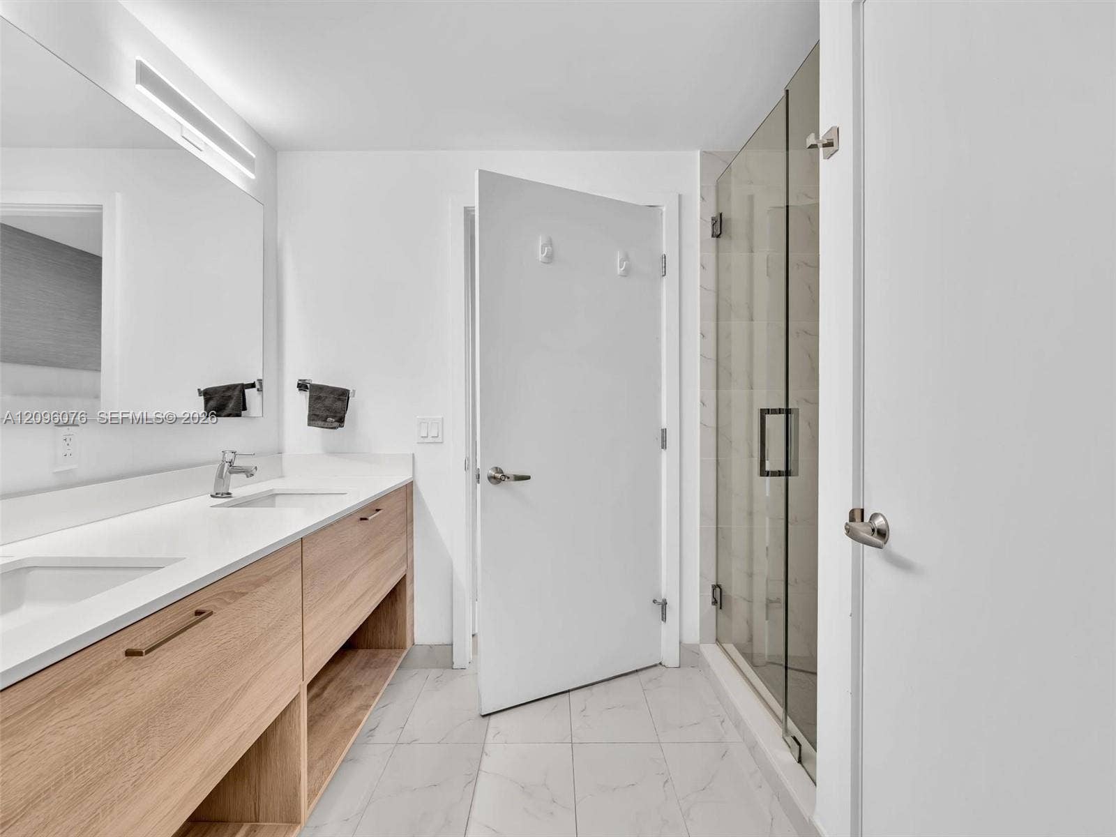 16385 Biscayne Boulevard, #1101, North Miami Beach, FL 33160 Bathroom featuring a dual-sink vanity with light wood-finish cabinetry, solid surface countertops, a full-width mirror, and a walk-in shower with a glass enclosure and tile flooring