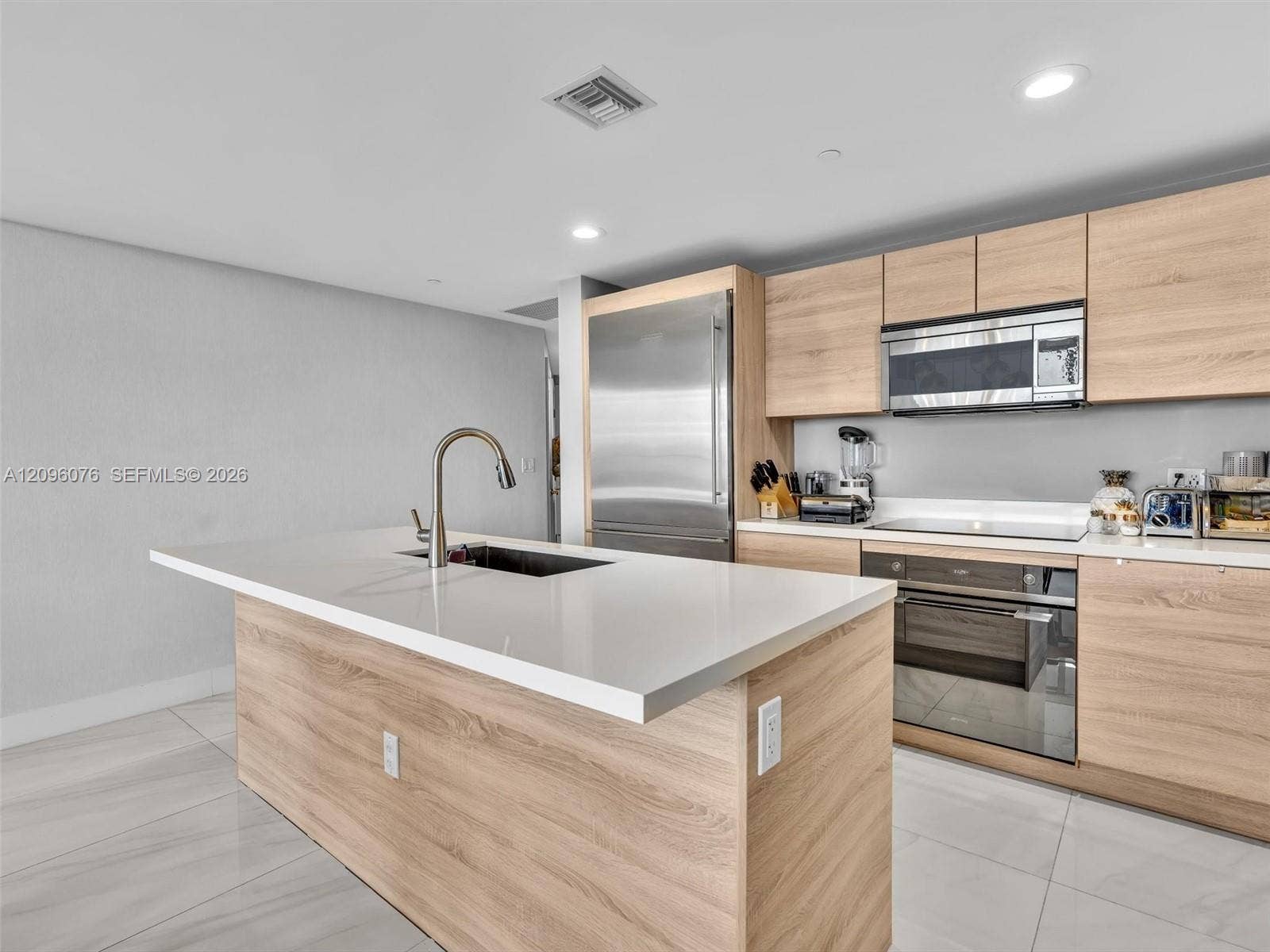 16385 Biscayne Boulevard, #1101, North Miami Beach, FL 33160 Kitchen featuring flat-panel wood-finish cabinetry, white composite countertops, a center island with an undermount sink, stainless steel appliances, and large-format tile flooring