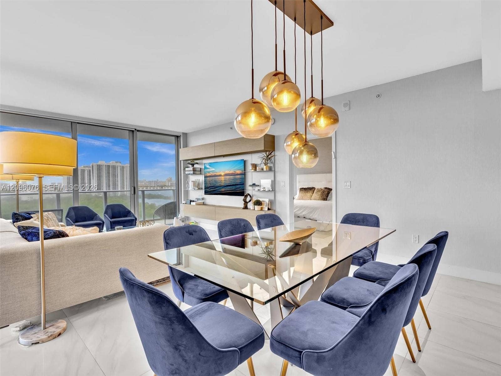 16385 Biscayne Boulevard, #1101, North Miami Beach, FL 33160 Open-concept living space featuring expansive floor-to-ceiling windows, polished stone-finish flooring, custom built-in media cabinetry, and a modern multi-pendant light fixture