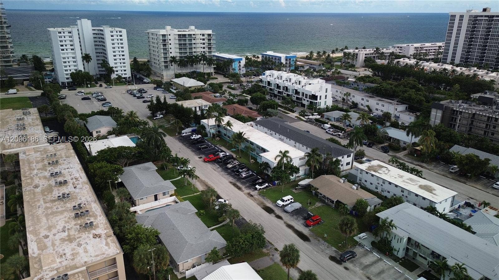 Aerial perspective featuring coastal proximity, multi-family residential structures, paved off-street parking areas, and mature palm trees