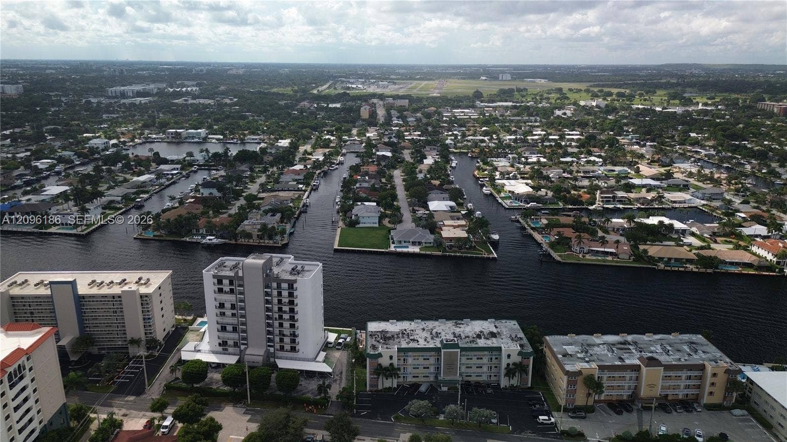 Aerial perspective of waterfront residential community featuring expansive canal systems, multi-story building structures, and paved parking surfaces