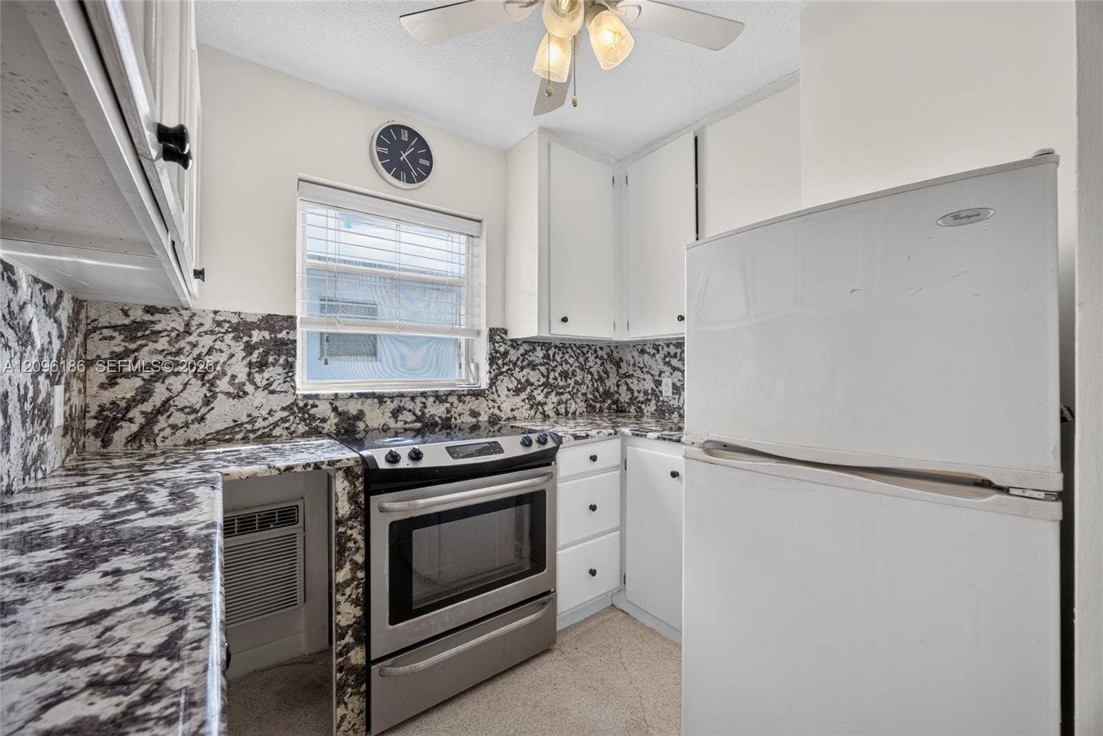 Kitchen featuring white shaker-style cabinetry, high-contrast patterned stone countertops and backsplash, stainless steel range, and ceiling-mounted light fixture