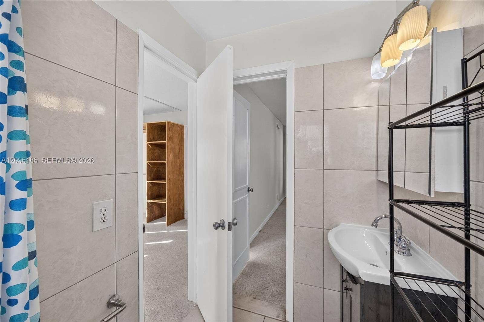 Bathroom featuring large-format ceramic wall tiling, a pedestal sink with a chrome finish faucet, a medicine cabinet with integrated lighting, and built-in shelving