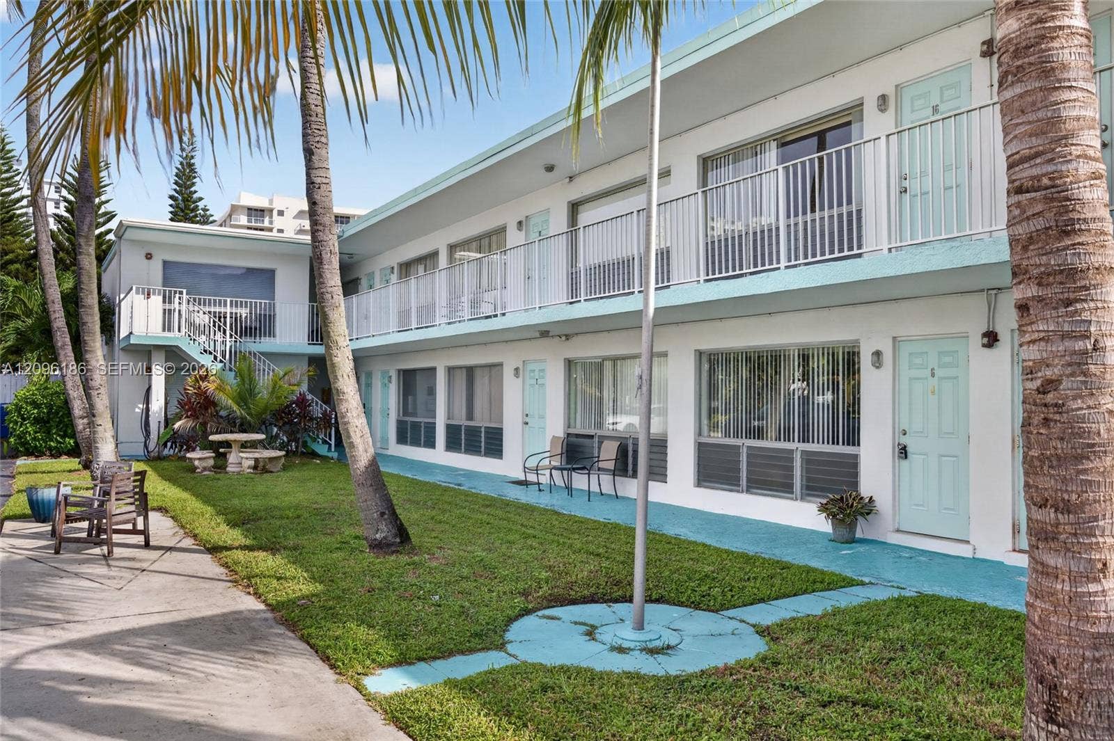 Two-story building exterior featuring smooth stucco siding, railed second-story balconies, expansive glass windows, and ground-level patios with painted concrete walkways