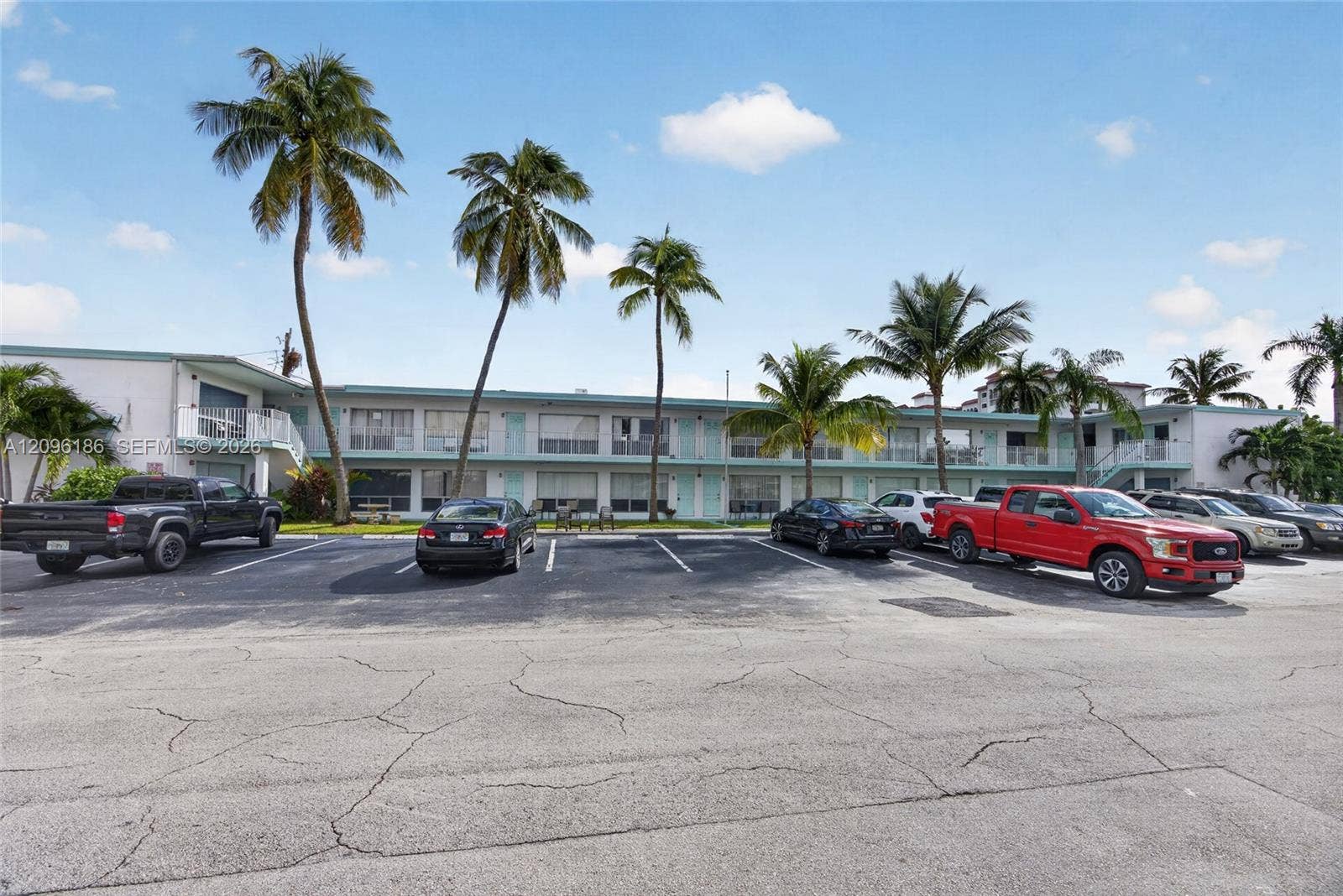 Multi-story residential building exterior featuring a white facade, covered walkways with metal railings, and established palm trees