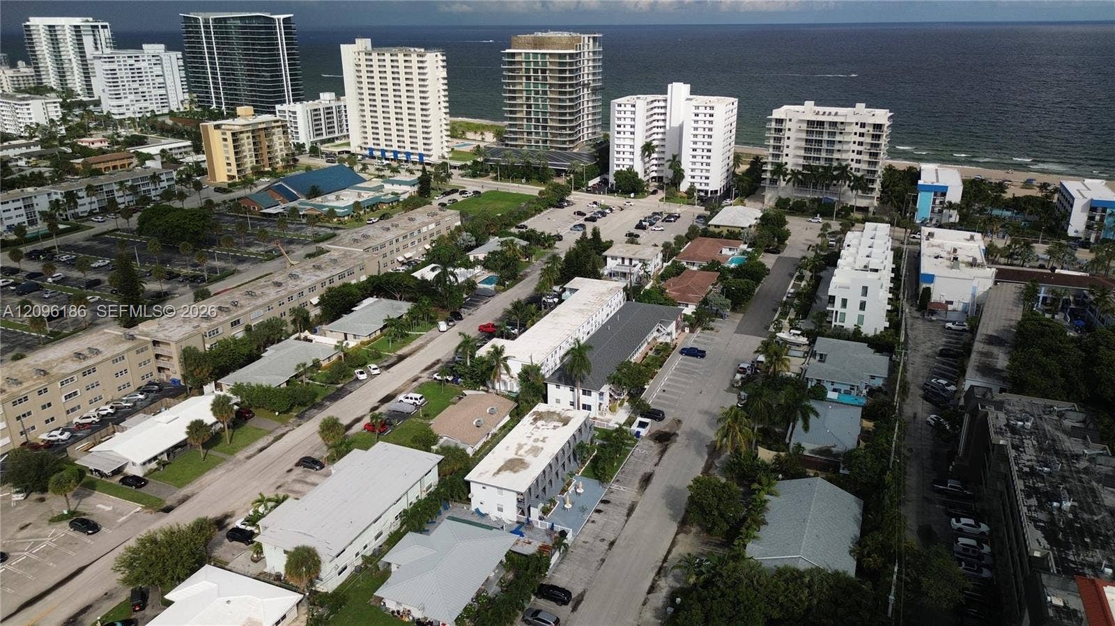 Aerial perspective featuring coastal proximity, multi-story building density, expansive paved parking lots, mature palm trees, and established street-level infrastructure