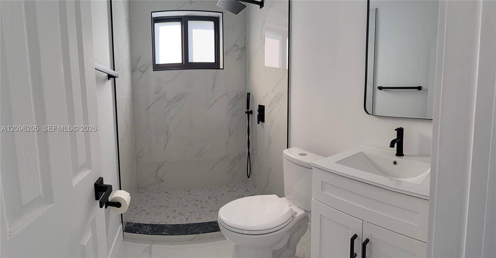 Bathroom featuring a walk-in shower with stone-patterned wall tile, a white vanity with a single basin, a matte black faucet, and a wall-mounted rectangular mirror