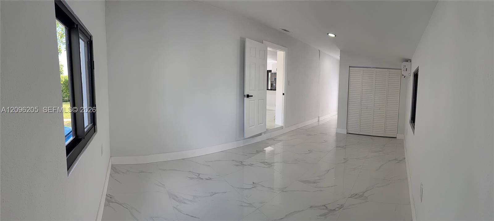 Interior space featuring polished stone-finish tile flooring, recessed ceiling lighting, a closet with white louvered doors, and a six-panel interior door