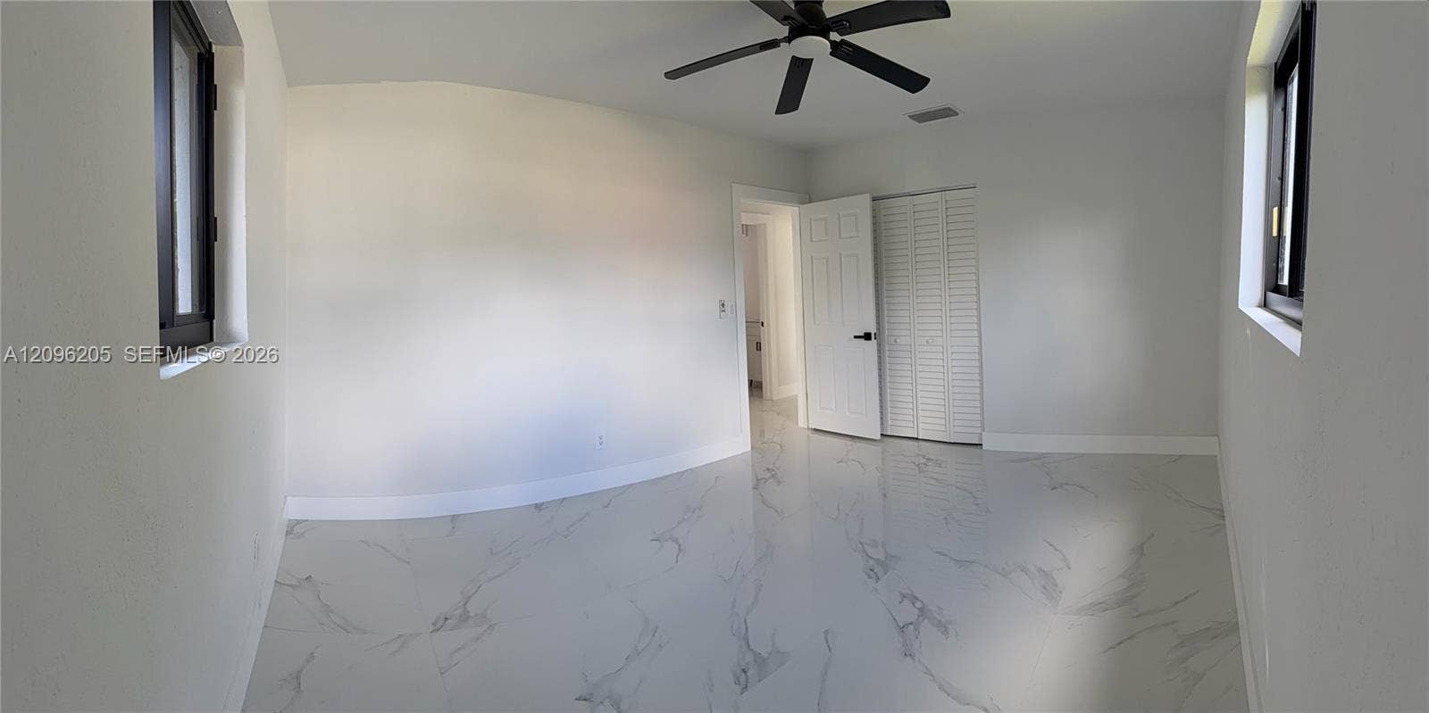 Interior room featuring large-format tile flooring with a neutral veined pattern, dual windows with dark frames, a ceiling fan, and a built-in closet with louvered doors