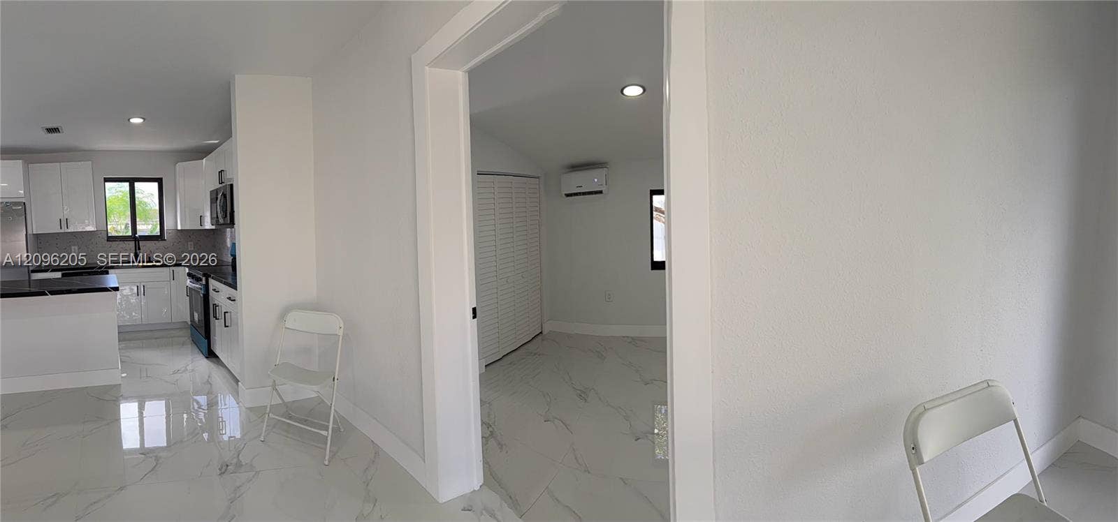 Interior space featuring polished stone-finish tile flooring, white shaker-style cabinetry, dark stone-finish countertops, recessed lighting, and a wall-mounted ductless climate control unit