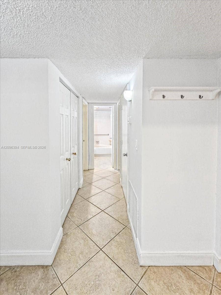 1830 Sabal Palm Drive, #105, Davie, FL 33324 Hallway featuring neutral-toned tile flooring set on a diagonal, dual-panel closet doors, and a wall-mounted hook rack