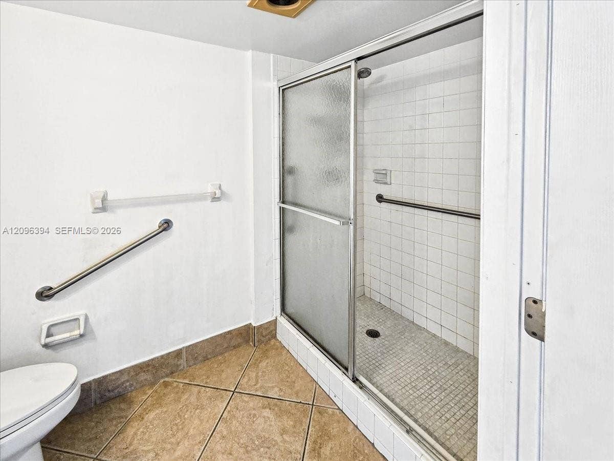 1830 Sabal Palm Drive, #105, Davie, FL 33324 Walk-in shower featuring a sliding glass door, tiled wall surround, and metal grab bars, paired with large-format ceramic floor tiling