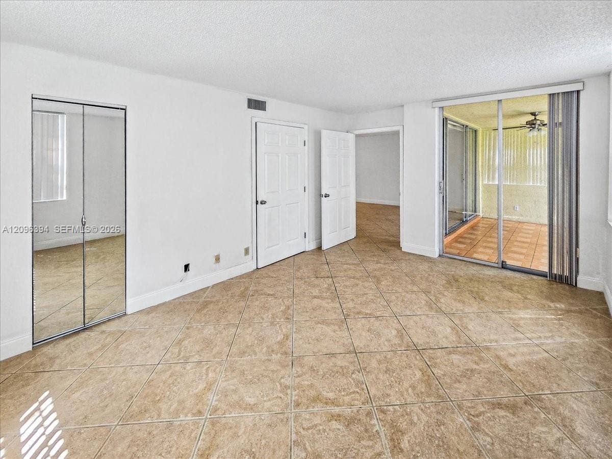 1830 Sabal Palm Drive, #105, Davie, FL 33324 Interior space featuring diagonal ceramic tile flooring, mirrored sliding closet doors, and a sliding glass door providing access to a screened enclosure