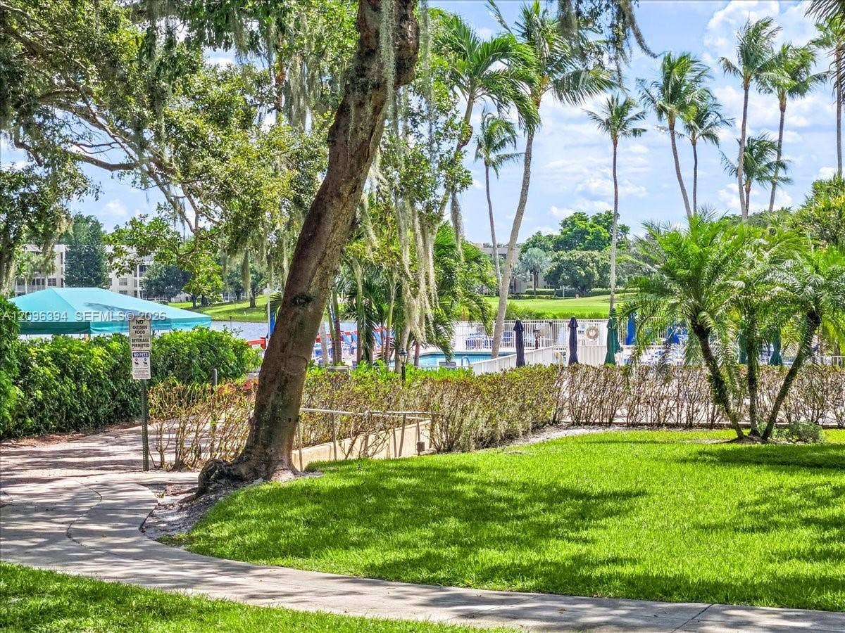 1830 Sabal Palm Drive, #105, Davie, FL 33324 Manicured lawn, mature trees with Spanish moss, paved walkway, tropical landscaping, and aquatic facility