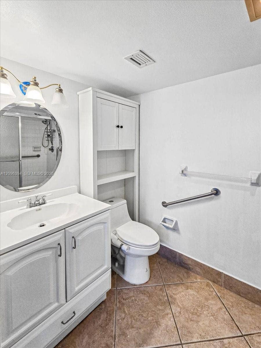 1830 Sabal Palm Drive, #105, Davie, FL 33324 Bathroom featuring a white vanity with integrated sink, circular mirror, built-in floor-to-ceiling storage cabinetry, tile flooring, and metallic wall-mounted safety bars