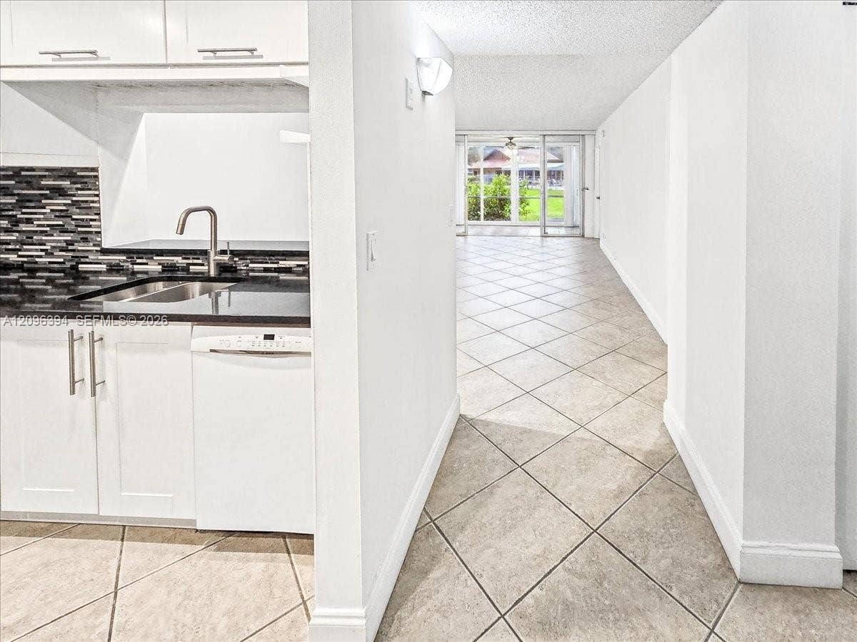 1830 Sabal Palm Drive, #105, Davie, FL 33324 Kitchen featuring white cabinetry, dark countertops, a mosaic tile backsplash, and stainless steel hardware, set against diagonal-set stone-finish tile flooring
