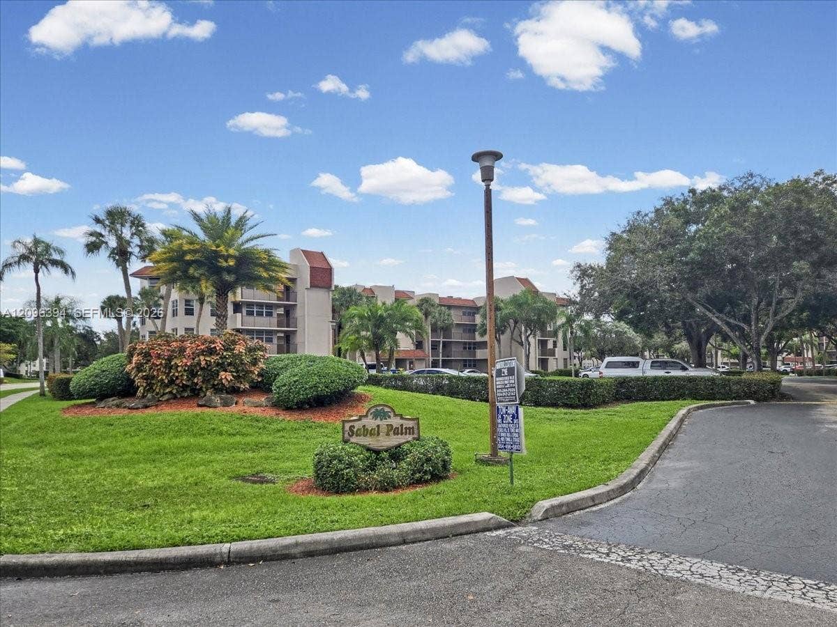 1830 Sabal Palm Drive, #105, Davie, FL 33324 Community grounds featuring mature palm trees, manicured landscaping, asphalt pathways, and multi-story residential structures
