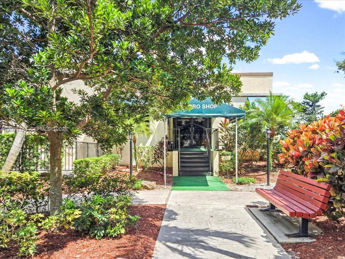 1830 Sabal Palm Drive, #105, Davie, FL 33324 Building entrance featuring an awning-covered staircase, concrete walkway, and landscaped grounds with mature trees and shrubbery