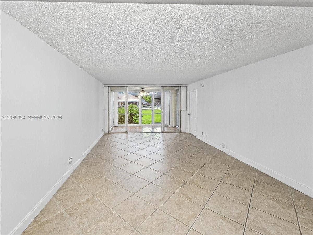 1830 Sabal Palm Drive, #105, Davie, FL 33324 Neutral-toned tile flooring, textured ceiling, and sliding glass doors with exterior access