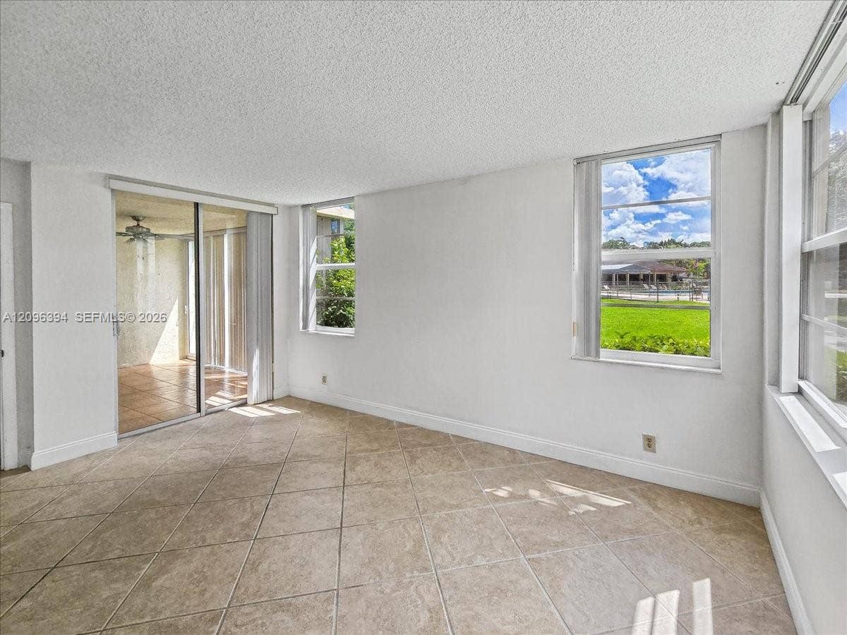 1830 Sabal Palm Drive, #105, Davie, FL 33324 Living area featuring neutral-tone tile flooring, sliding glass doors, and multiple windows providing natural light