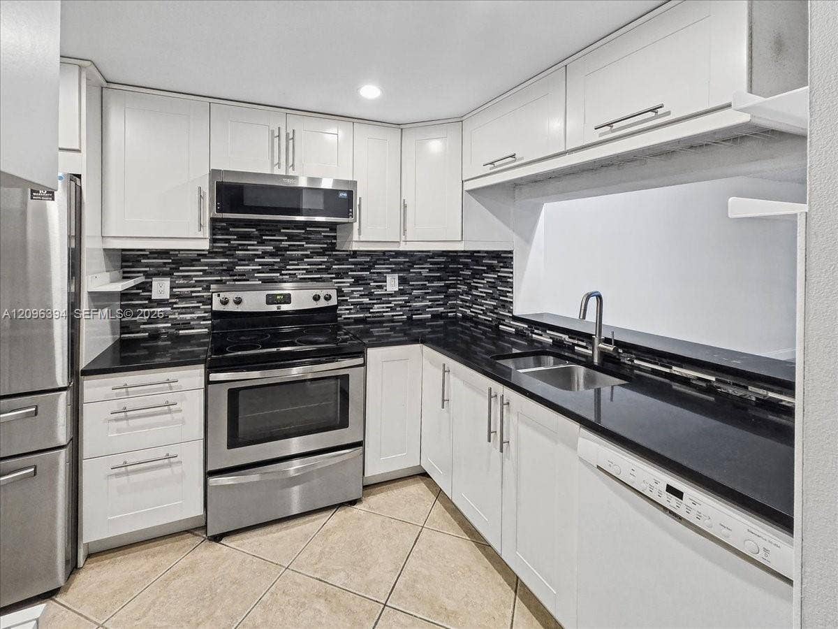 1830 Sabal Palm Drive, #105, Davie, FL 33324 Kitchen featuring white shaker-style cabinetry, black solid-surface countertops, stainless steel appliances, a multi-tonal mosaic tile backsplash, and tile flooring