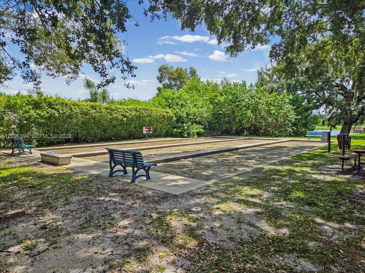 1830 Sabal Palm Drive, #105, Davie, FL 33324 Bocce ball court featuring a rectangular sand playing surface, timber border edging, concrete perimeter walkways, and mature tree-lined surroundings