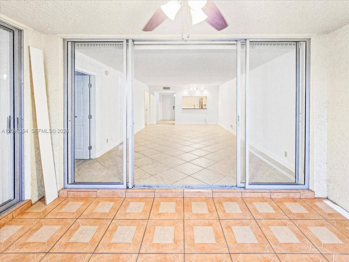 1830 Sabal Palm Drive, #105, Davie, FL 33324 Triple-panel sliding glass doors with brushed metal frames, ceramic tile flooring, and ceiling fan with integrated lighting