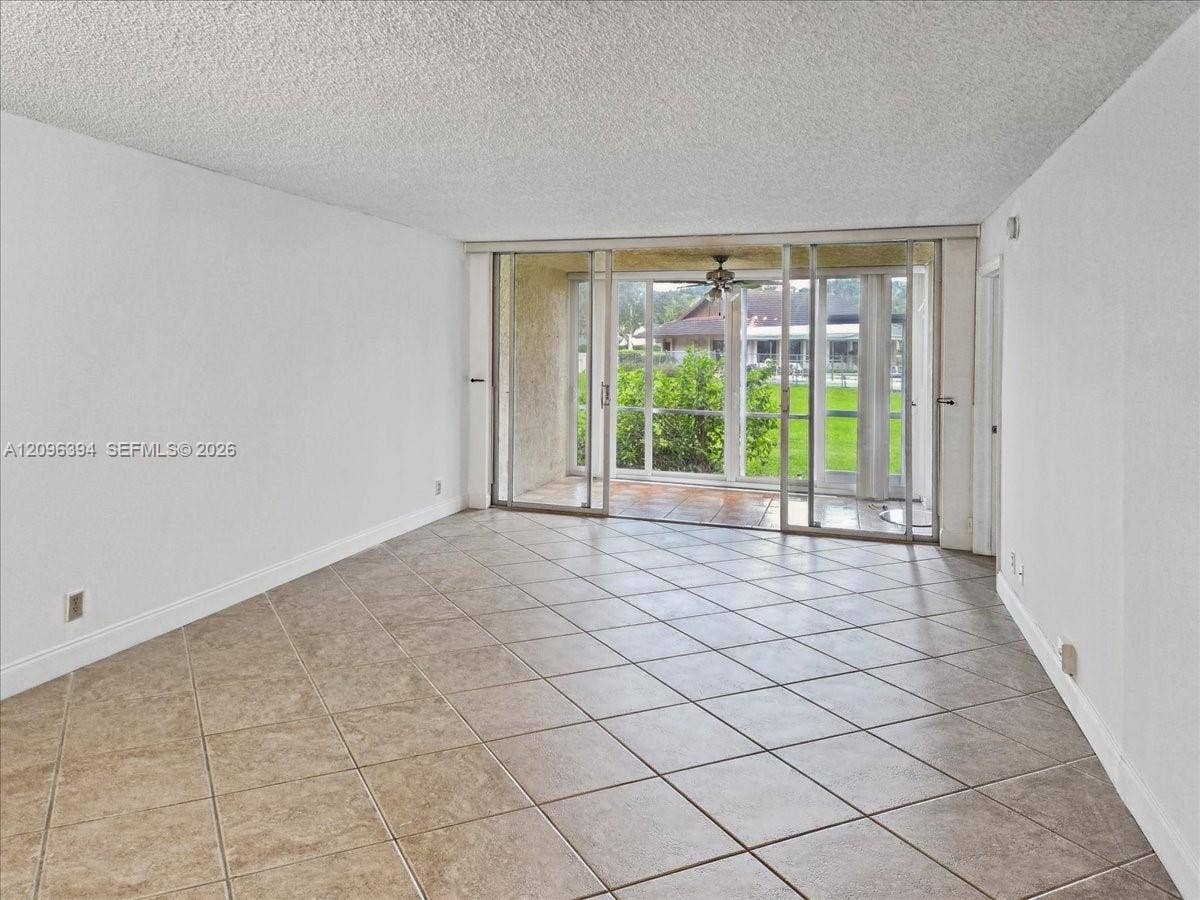 1830 Sabal Palm Drive, #105, Davie, FL 33324 Open-concept interior featuring large-format diagonal tile flooring, textured ceiling, and floor-to-ceiling glass sliding doors opening to a covered patio