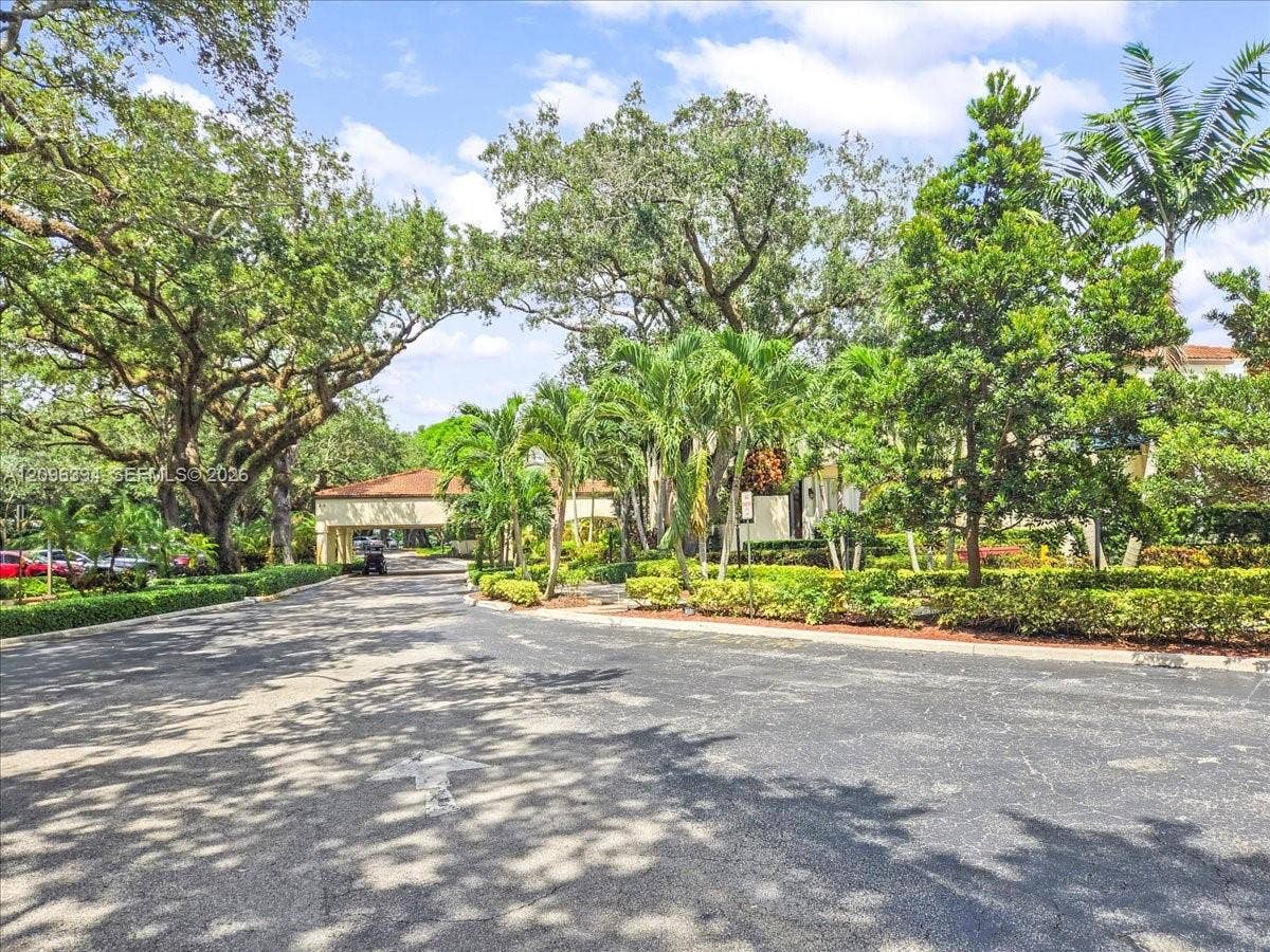 1830 Sabal Palm Drive, #105, Davie, FL 33324 Asphalt driveway entrance featuring mature oak trees, tropical palm landscaping, and a covered porte-cochre