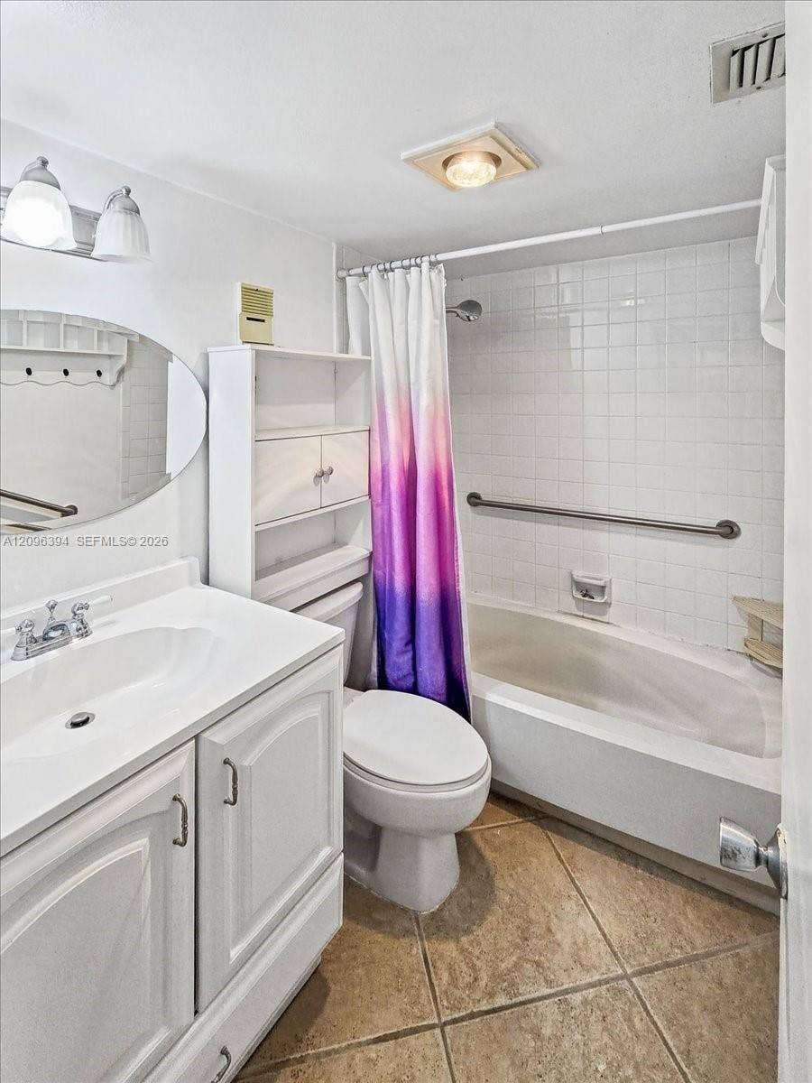 1830 Sabal Palm Drive, #105, Davie, FL 33324 Bathroom featuring a white vanity cabinet, dual-handle faucet, oval wall mirror, tile-surround bathtub with a metal grab bar, and neutral-toned tile flooring
