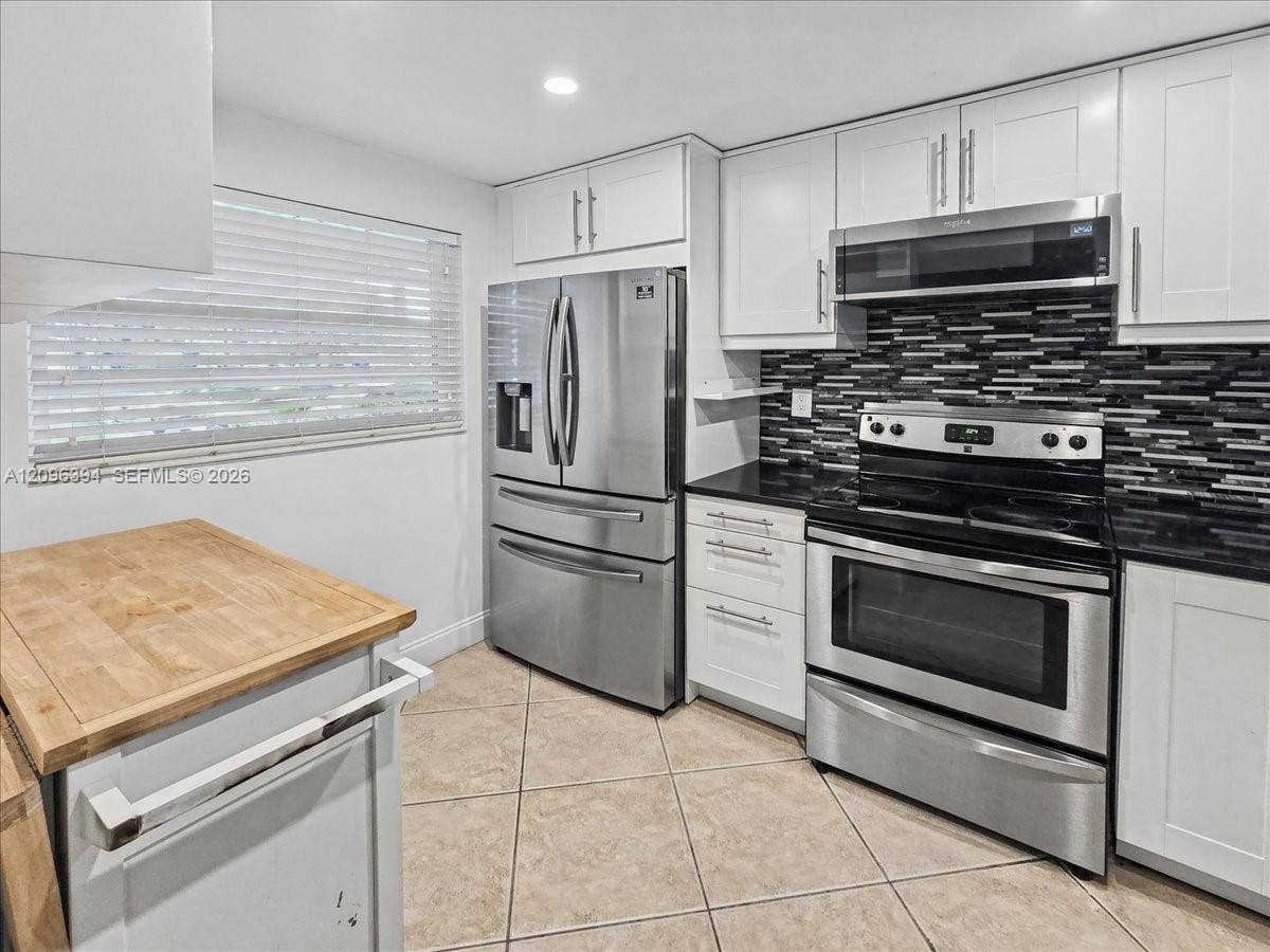 1830 Sabal Palm Drive, #105, Davie, FL 33324 Kitchen featuring white shaker-style cabinetry, stainless steel appliances, a linear tile backsplash, dark solid-surface countertops, and a wood-top kitchen island