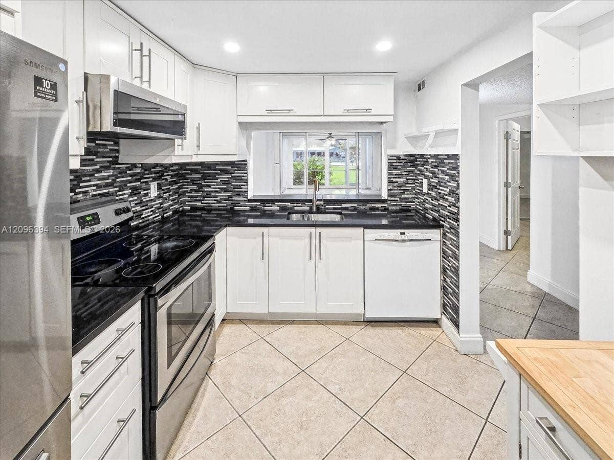 1830 Sabal Palm Drive, #105, Davie, FL 33324 Kitchen featuring white shaker-style cabinetry, dark stone countertops, decorative multi-tonal backsplash, stainless steel appliances, and ceramic tile flooring