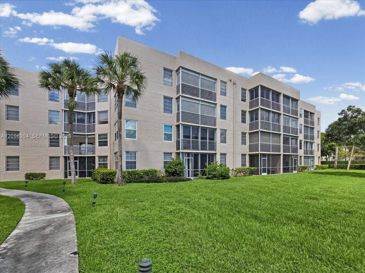 1830 Sabal Palm Drive, #105, Davie, FL 33324 Multi-story residential building featuring a stucco exterior, screened balconies, and a concrete walkway set within a landscaped lawn