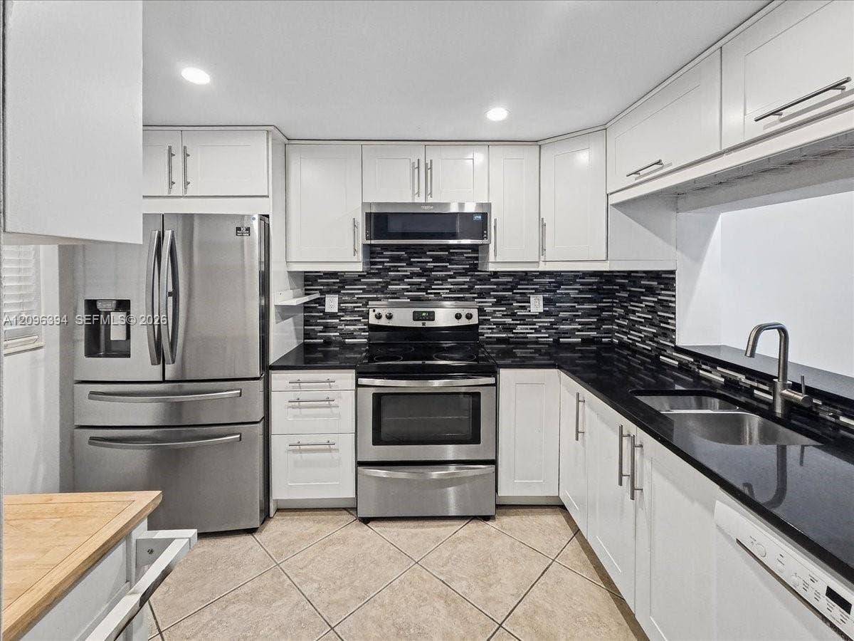 1830 Sabal Palm Drive, #105, Davie, FL 33324 Kitchen featuring white shaker-style cabinetry, dark stone countertops, stainless steel appliances, a mosaic tile backsplash, and recessed lighting