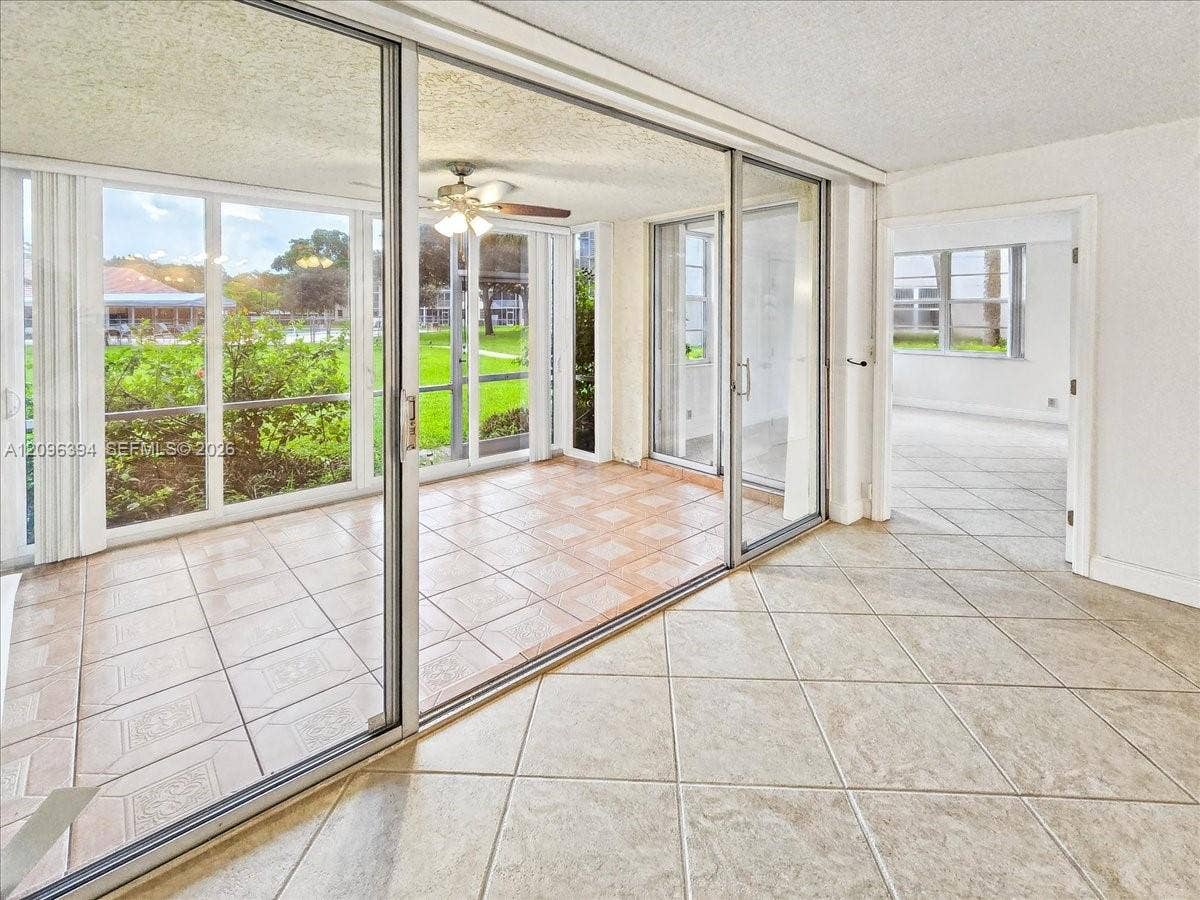 1830 Sabal Palm Drive, #105, Davie, FL 33324 Enclosed sunroom featuring expansive glass sliding doors, neutral tile flooring, and a ceiling fan