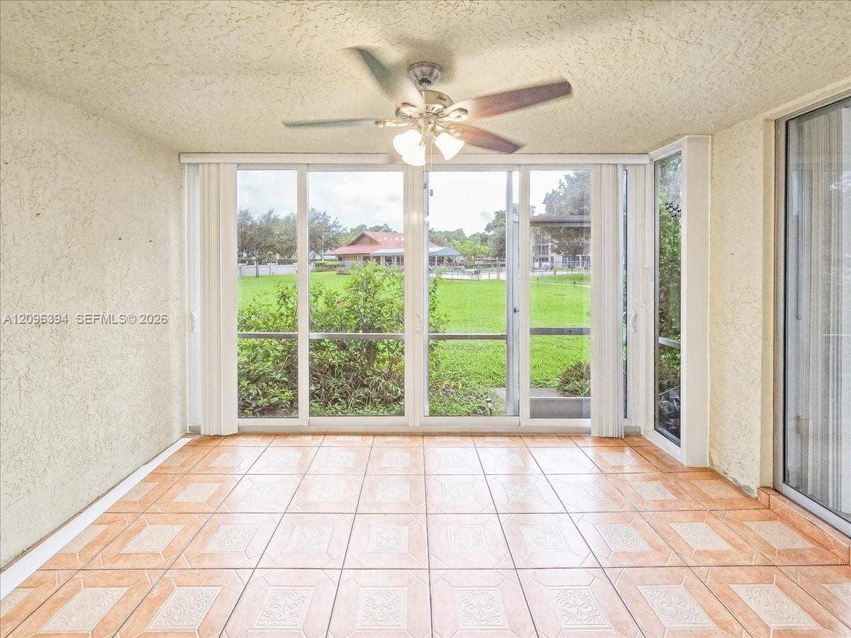 1830 Sabal Palm Drive, #105, Davie, FL 33324 Enclosed sunroom featuring ceramic tile flooring, textured ceilings, a multi-blade ceiling fan with integrated lighting, and expansive glass sliding door panels