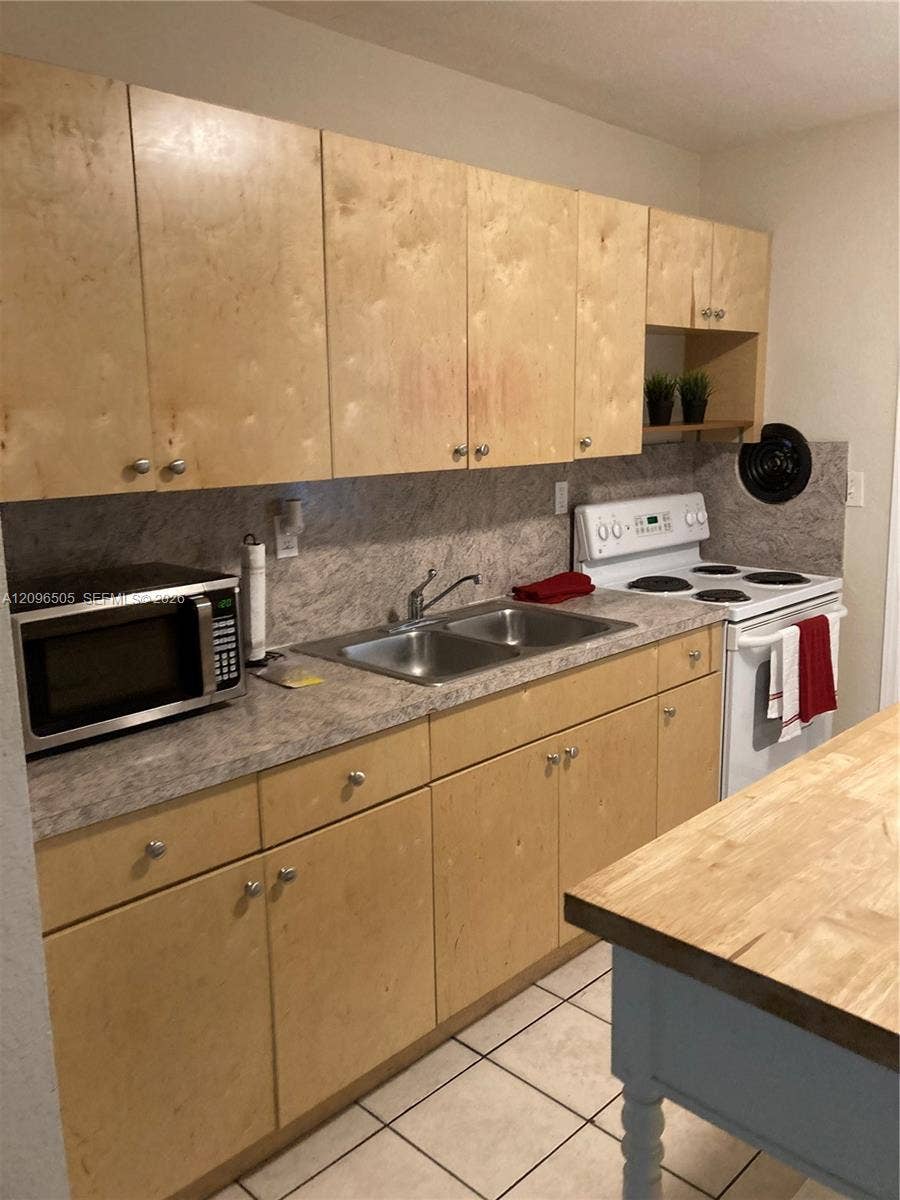 Light-toned wood cabinetry with round hardware, stone-finish laminate countertops, stainless steel dual-basin sink, and tile flooring