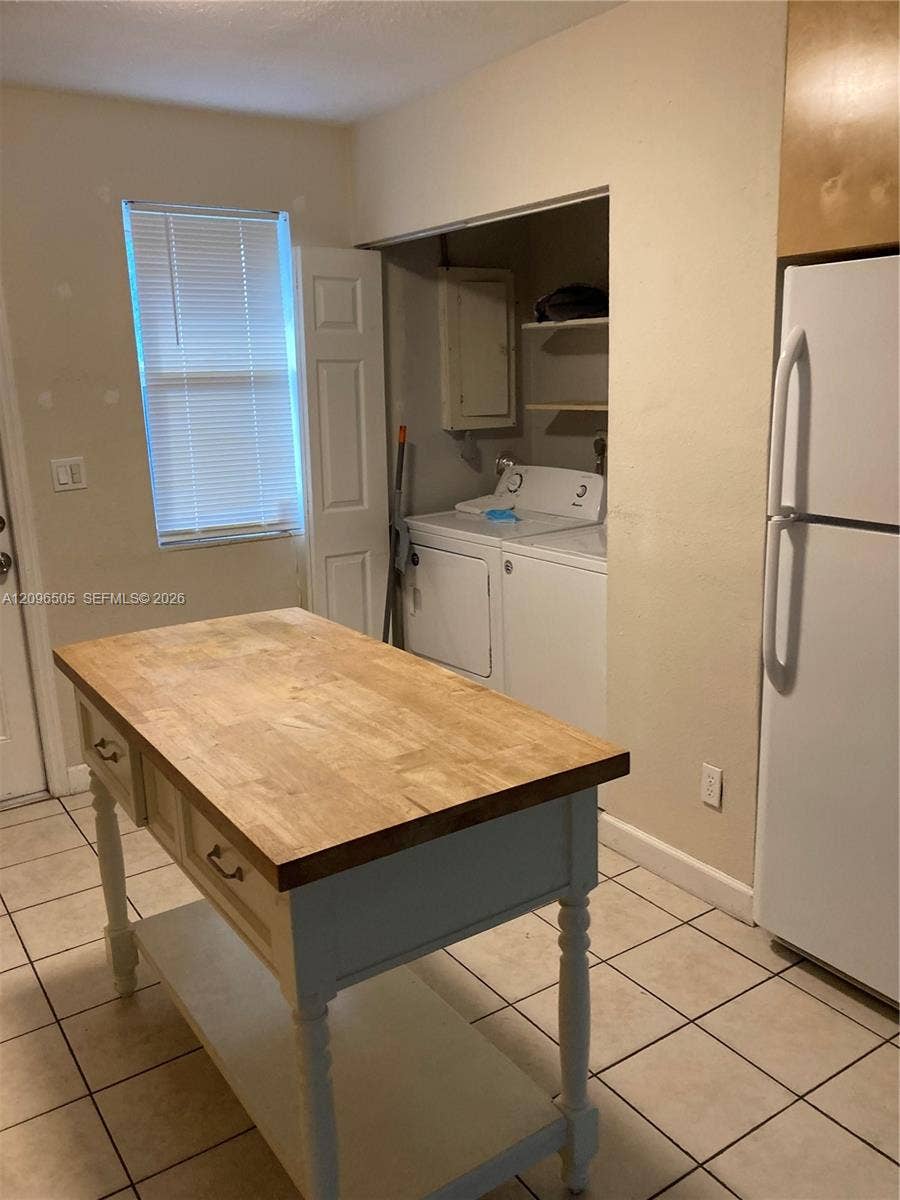 Built-in laundry area with shelving, tile flooring, and a kitchen island featuring a wood-finish countertop