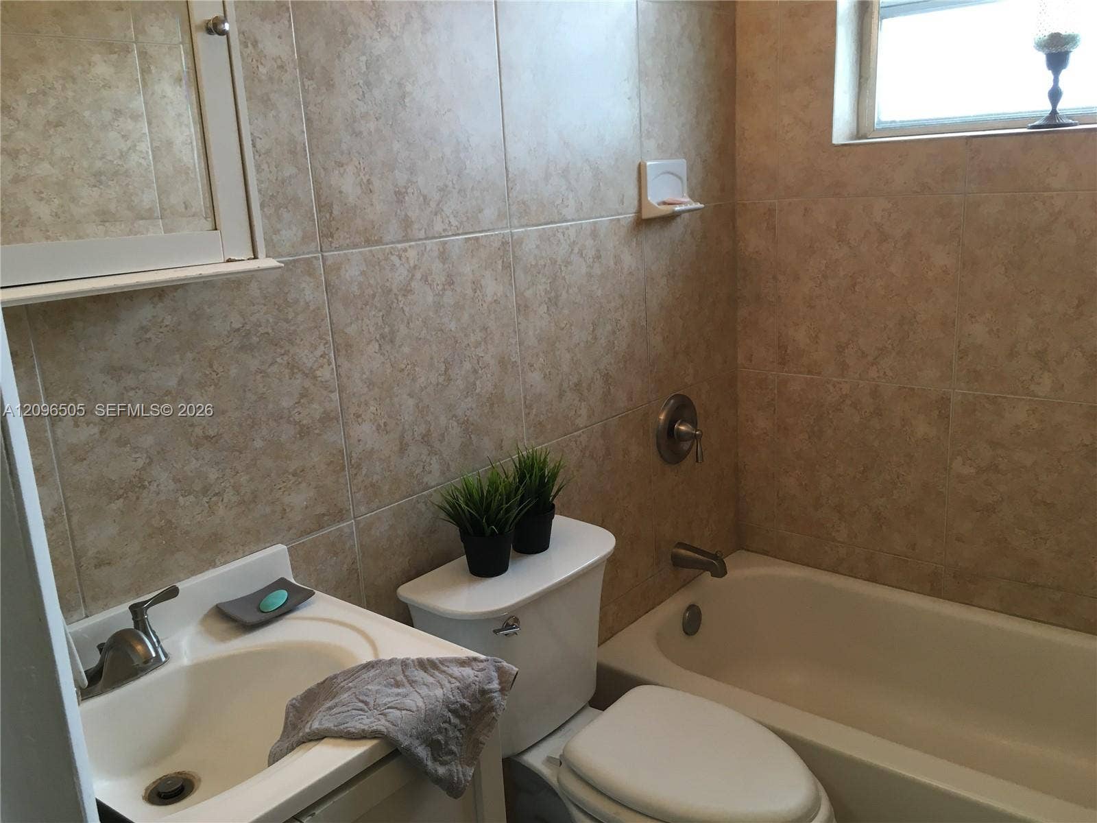 Bathroom featuring floor-to-ceiling neutral ceramic wall tiling, a built-in tub with shower hardware, a recessed medicine cabinet, and a single-basin vanity