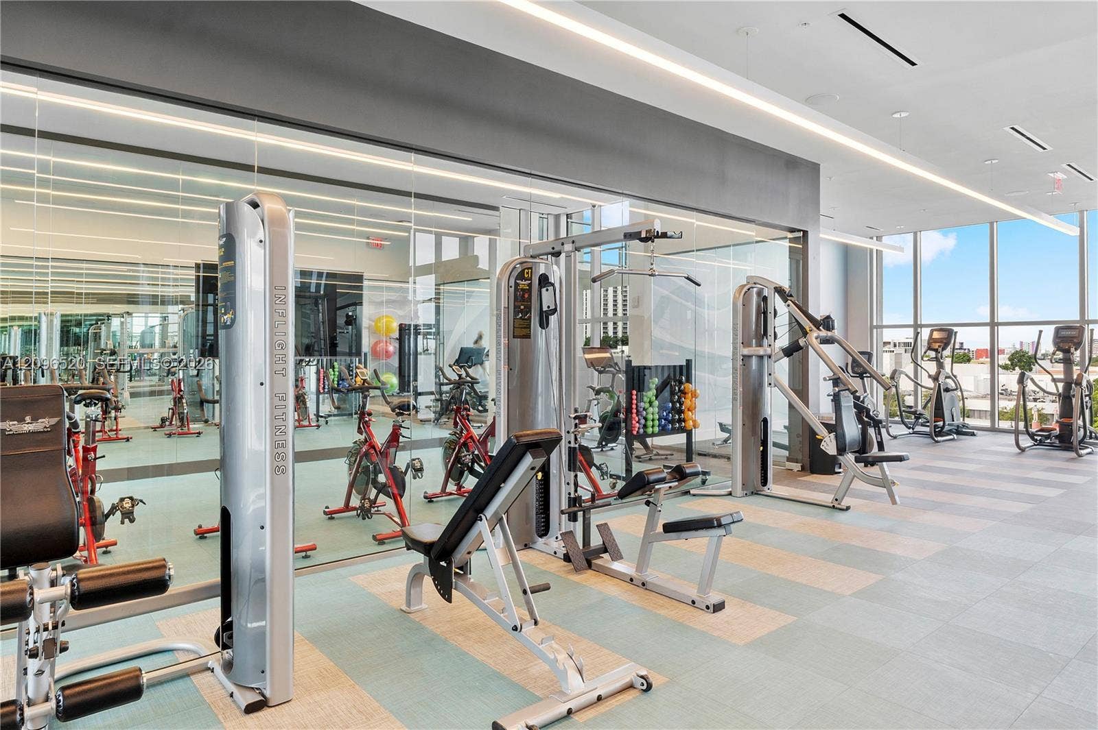 Fitness center featuring floor-to-ceiling windows, mirrored walls, recessed linear lighting, and large-format tile flooring