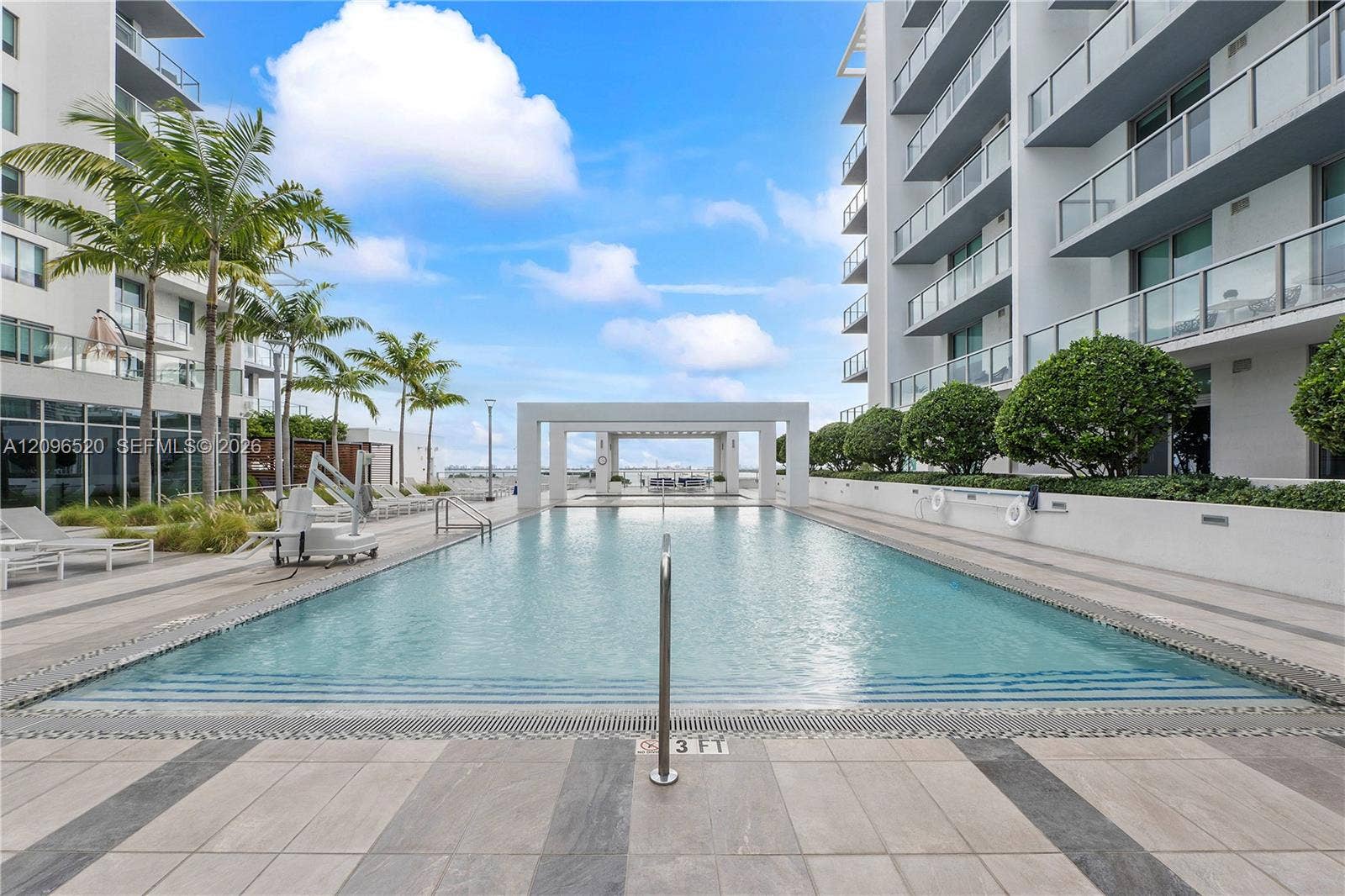 Swimming pool with a stone-paver deck, pergola structure, manicured landscaping, and building exterior featuring glass-railed balconies