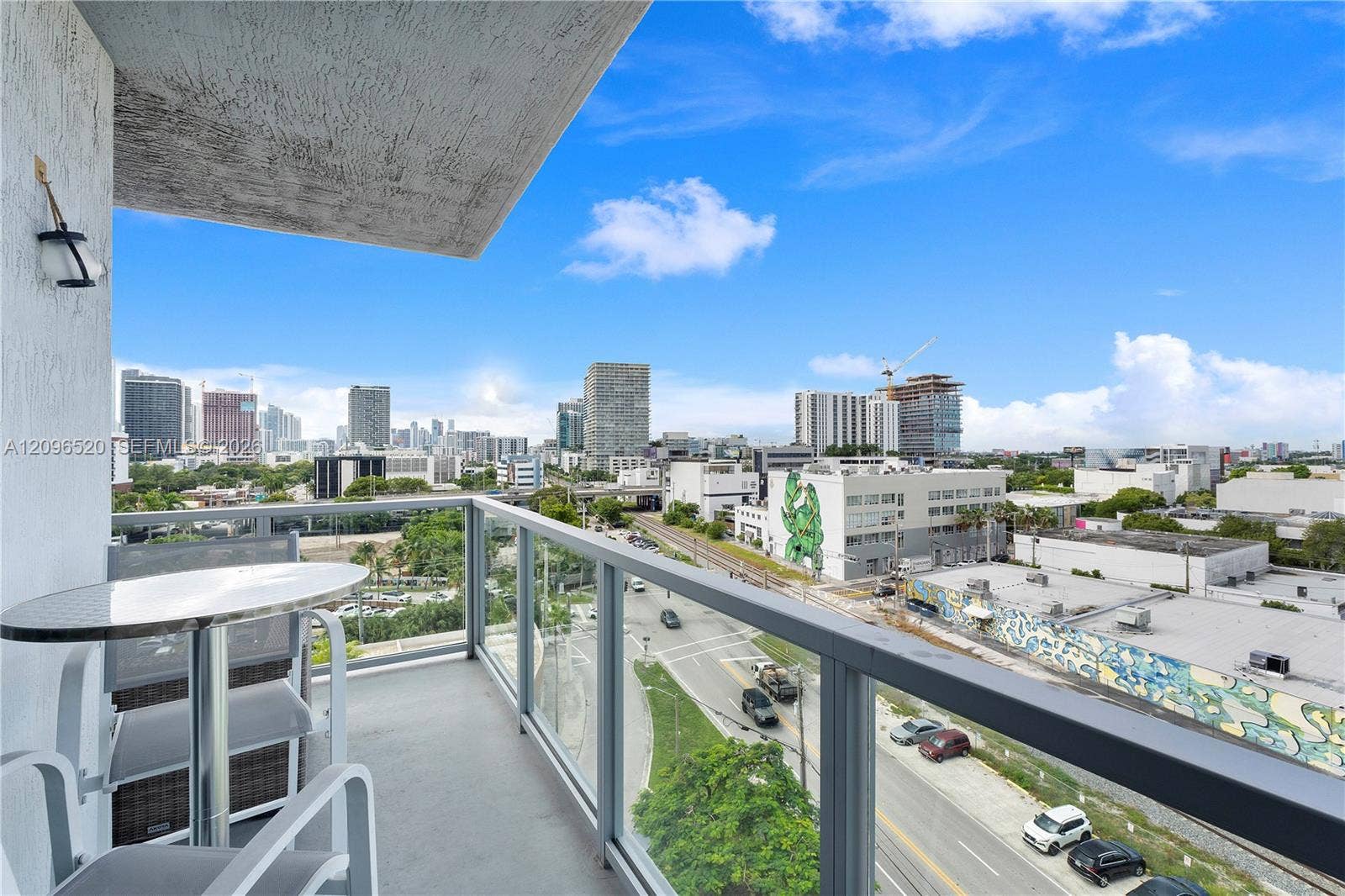 Covered balcony featuring concrete flooring, a wall-mounted light fixture, and a glass-paneled railing