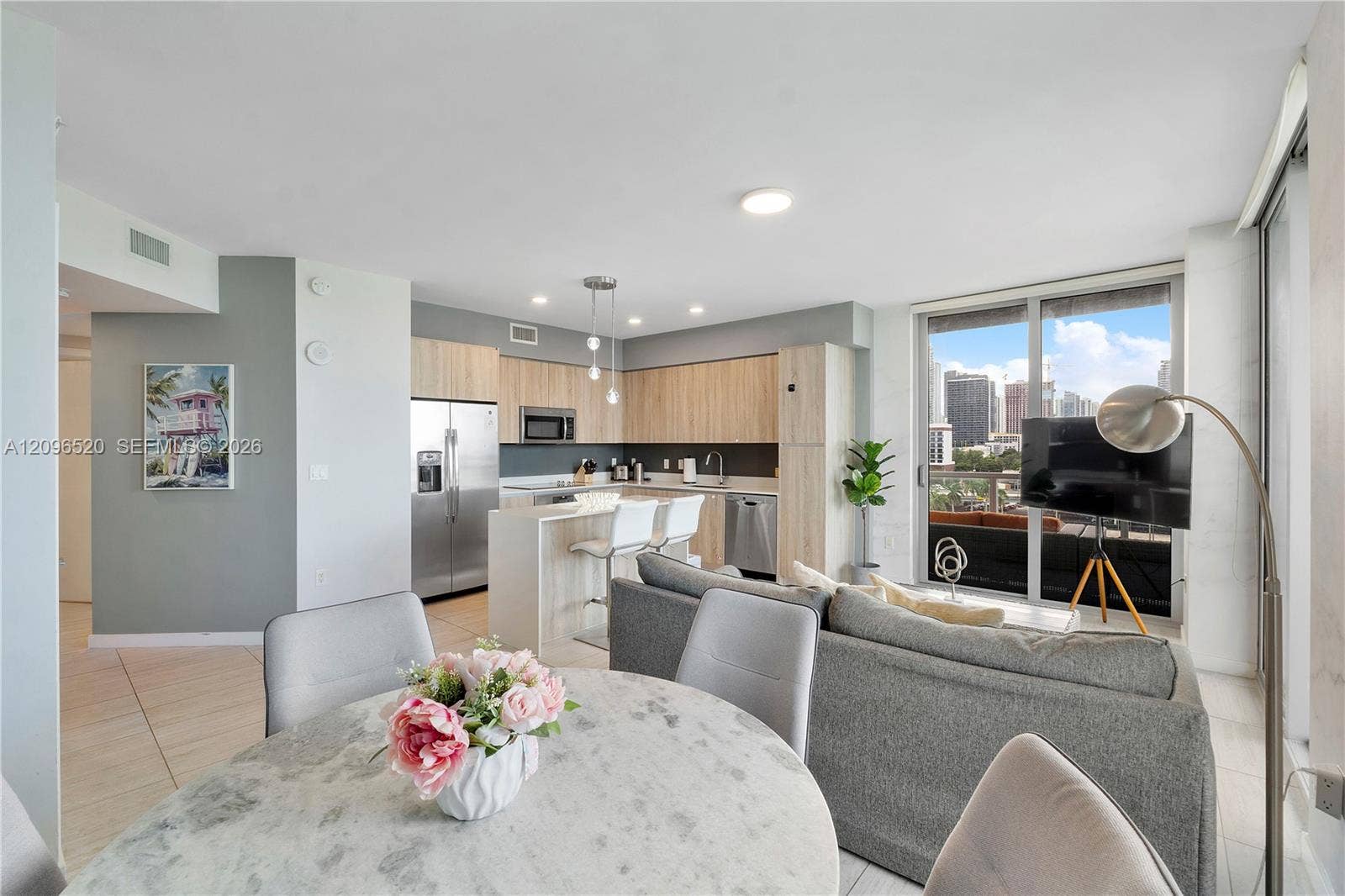Kitchen featuring light wood-finish cabinetry, stone-surfaced waterfall island, stainless steel appliances, and floor-to-ceiling glass sliding doors