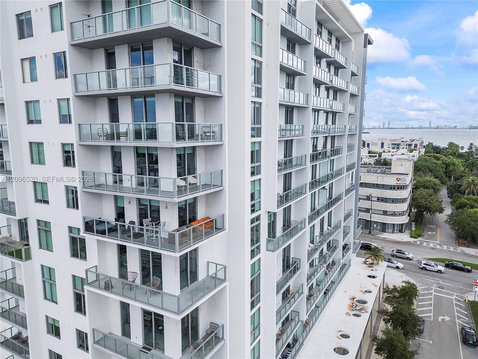 High-rise residential exterior featuring stacked private glass-railed balconies, floor-to-ceiling windows, and white concrete facade