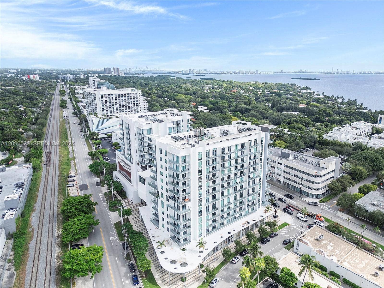 Multi-story residential building with a white exterior, expansive glass-railed balconies, ground-level covered walkways, and integrated palm tree landscaping
