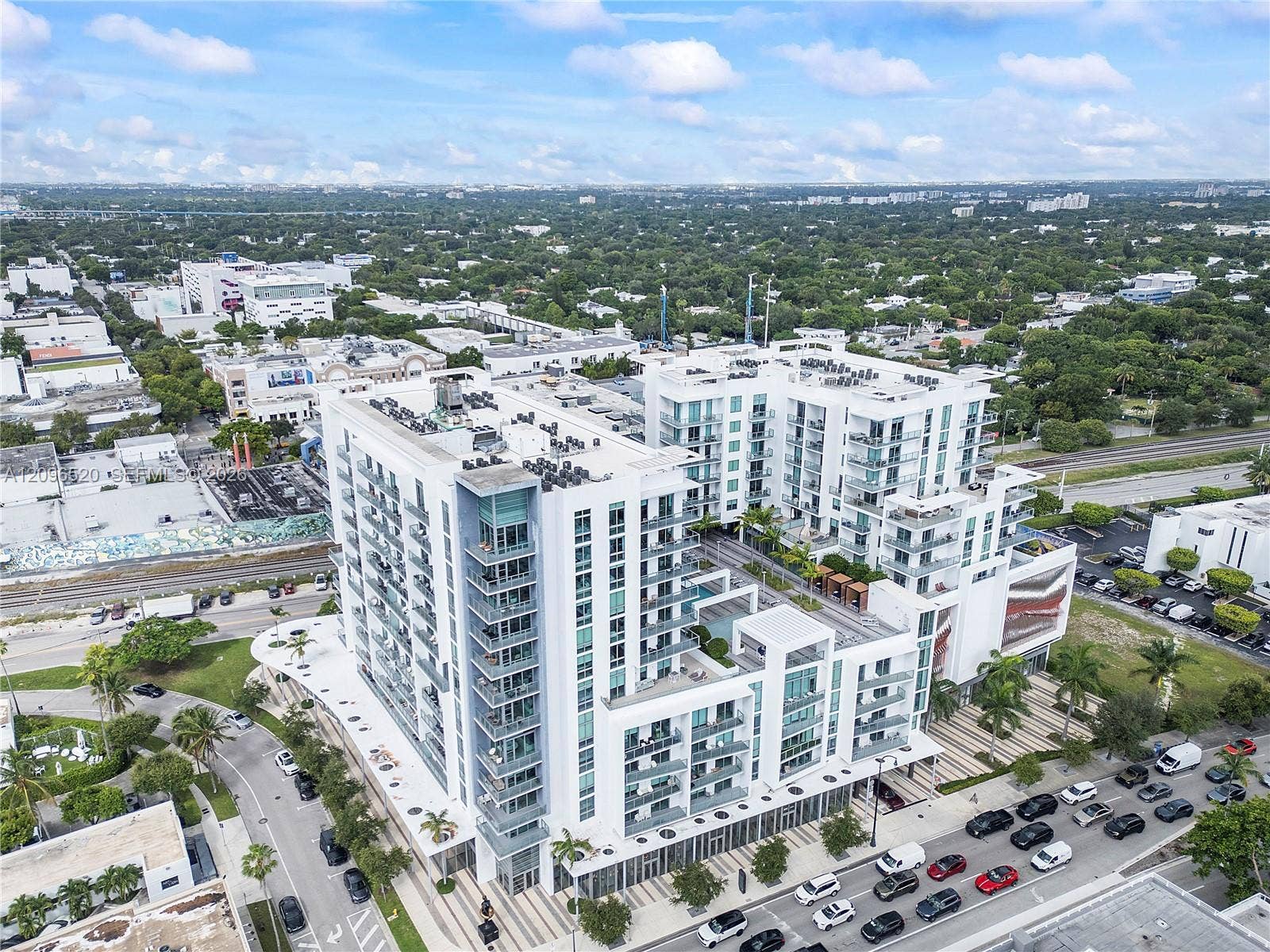 Multi-story residential building featuring a modern white facade, private balconies with glass railings, a landscaped courtyard deck, and ground-level paved pedestrian walkways