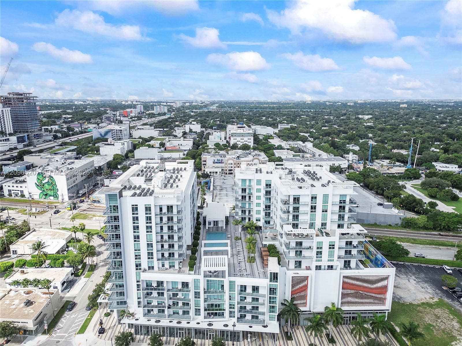 Multi-story mid-rise structure featuring private balconies, an expansive elevated terrace, a rooftop pool, and architectural facade accents