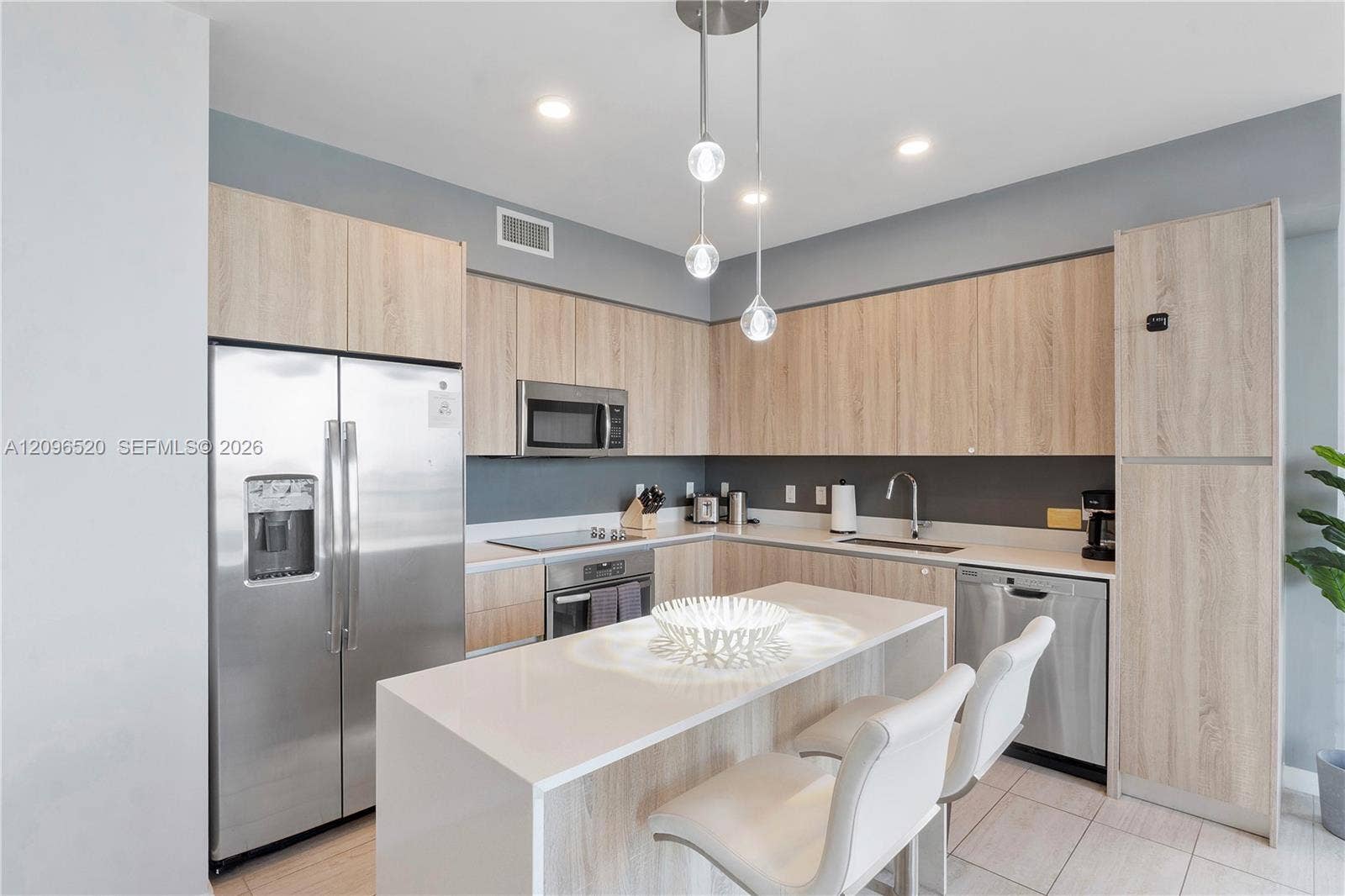 Kitchen featuring light wood-finish cabinetry, white solid-surface countertops, stainless steel appliances, a central island, and modern pendant lighting