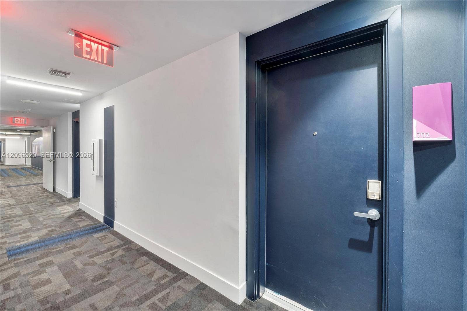 Dark-finished entry door with integrated electronic lock, patterned carpeted flooring, and neutral wall surfaces