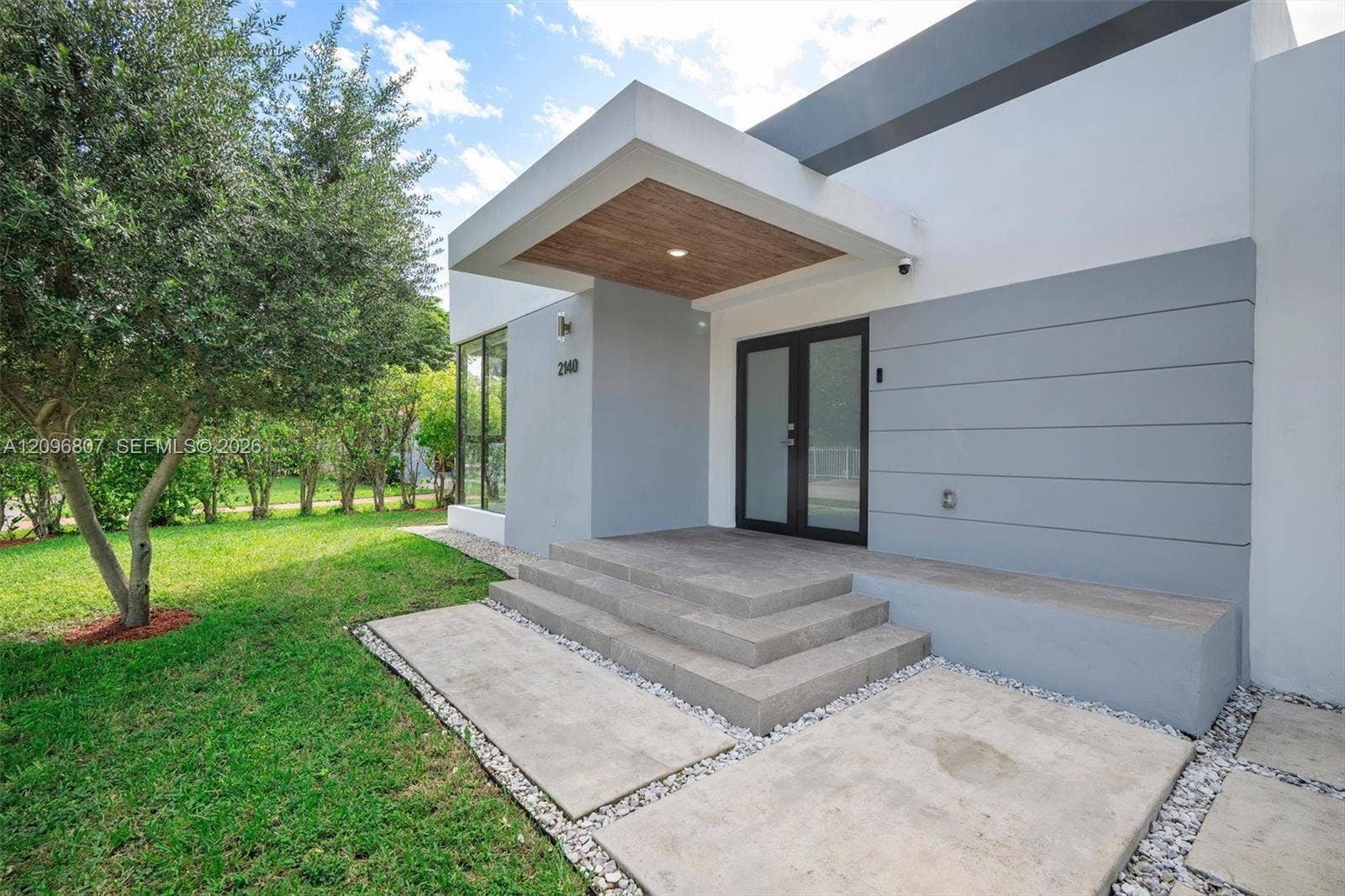 Modern facade featuring a cantilevered entryway with a wood-finish ceiling, concrete front steps, dual-glass entry doors, and horizontal panel siding
